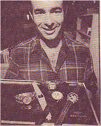Man in plaid shirt holding a tray containing five pre-owned Breitling watches.