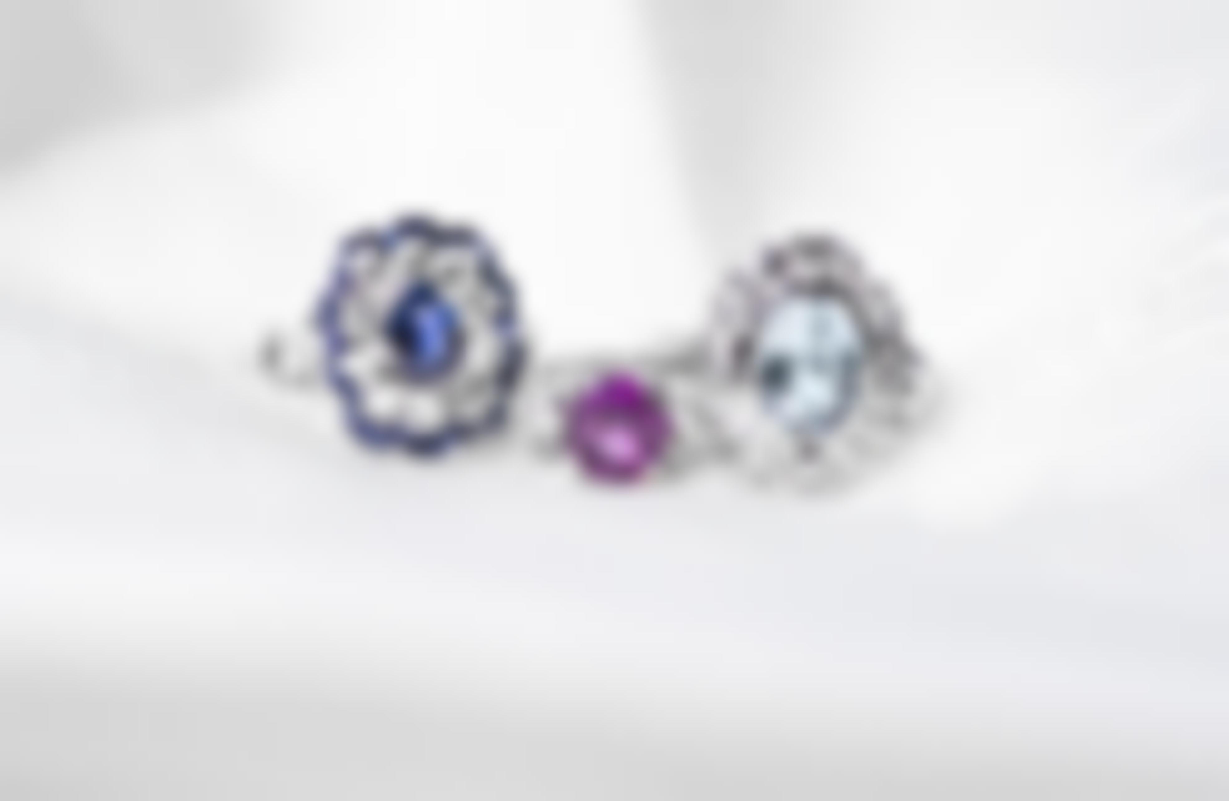 Three white gold engagement rings centered with colored gemstones on a white background.