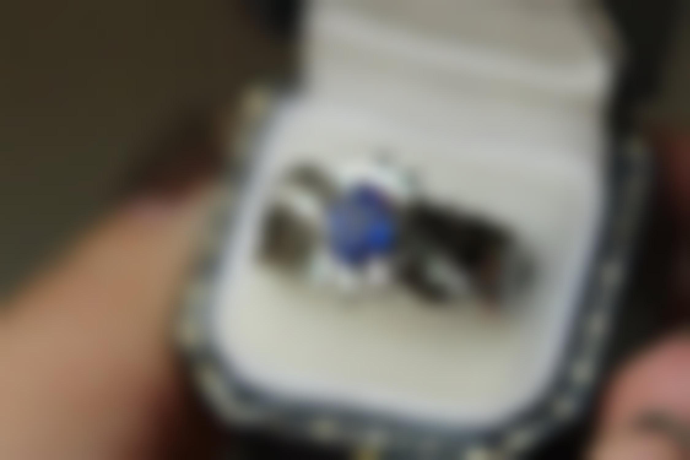 White gold engagement ring centered with a blue sapphire surrounded by a half-halo of diamond and diamonds in the band.