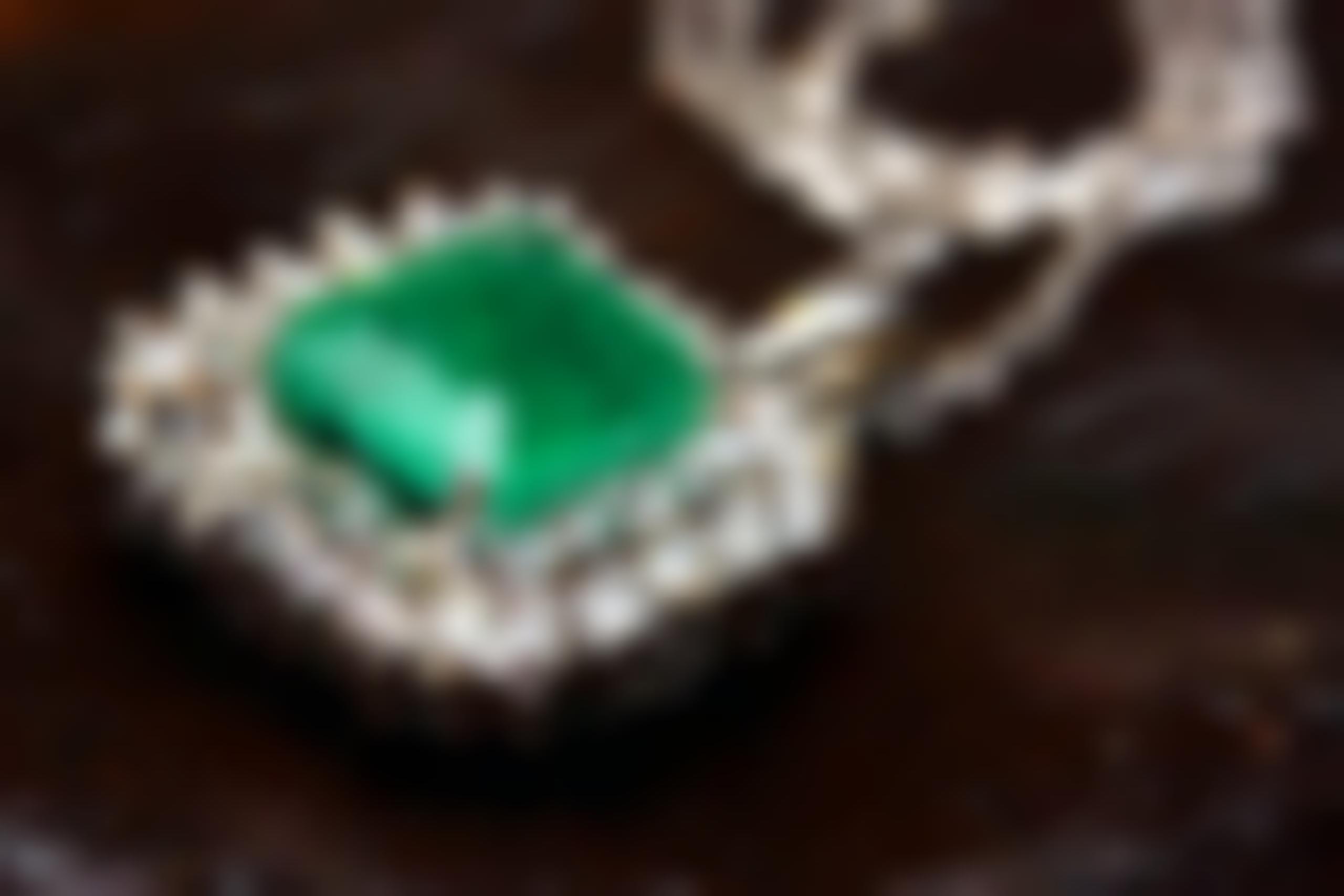 Antique white gold pendant centered with an emerald surrounded by a double diamond halo.