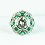 Antique platinum statement ring centered with a diamond surrounded by diamonds and emeralds.