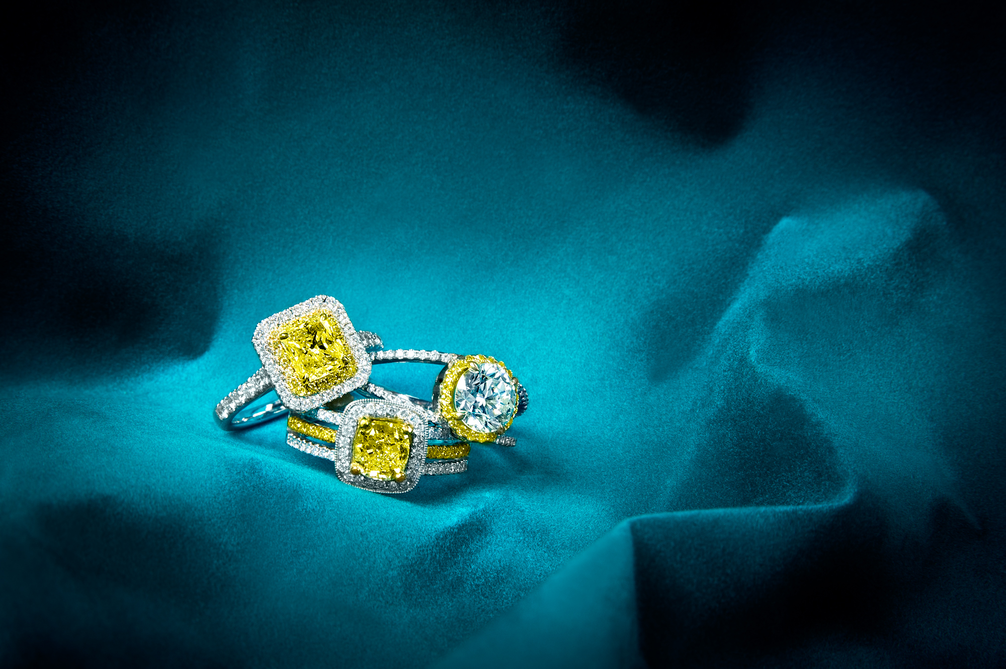 Three white gold engagement rings centered with yellow diamonds surrounded by white diamonds.