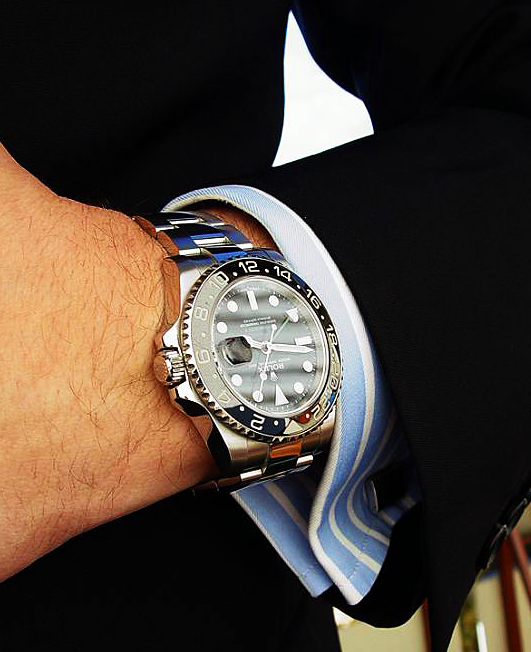 Man in a formal black suit showing rolex watch on his hands