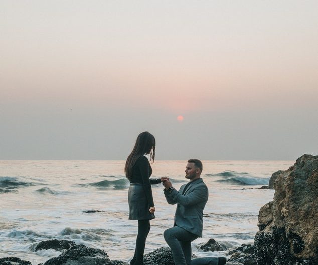 Man proposing to a woman on the beach at sunset.
