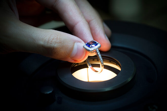 Jeweler holding a white gold purple gemstone ring over heat source.