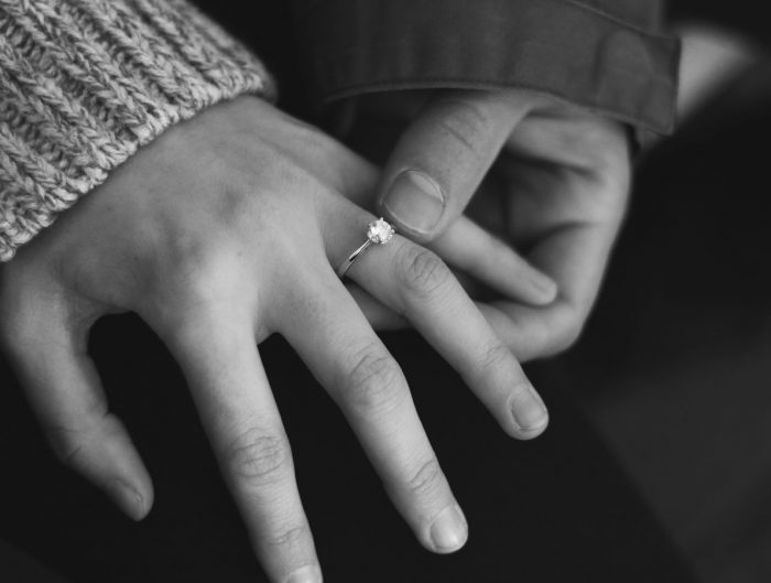 Close-up of a man putting an engagement ring on his fiancé’s ring finger.