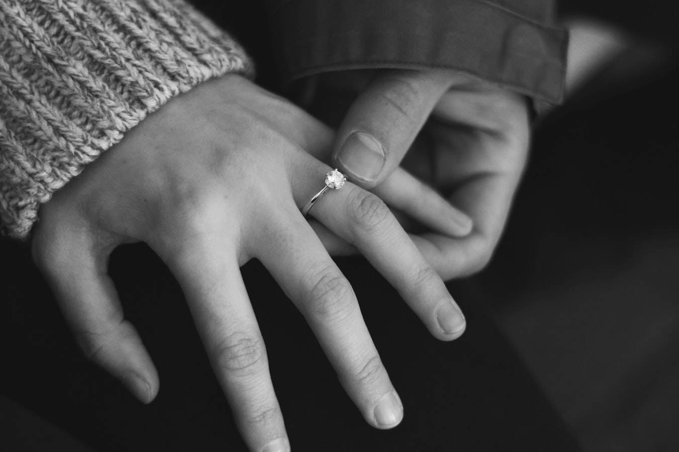 Close-up of a man putting an engagement ring on his fiancé’s ring finger.