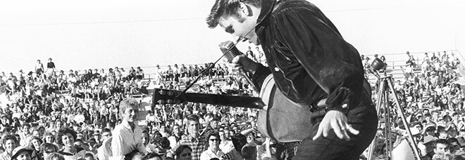 Elvis performing in front of crowd at an outdoor venue.