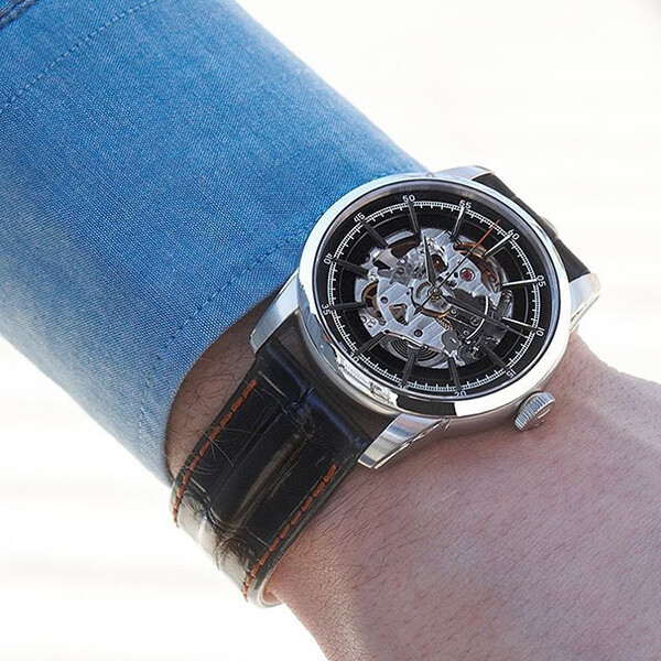 Man’s wrist featuring a Hamilton watch in stainless steel with an exhibition face and black leather strap.