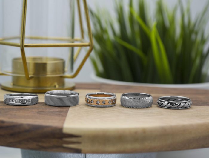 Five men’s wedding bands lined up on wooden table.
