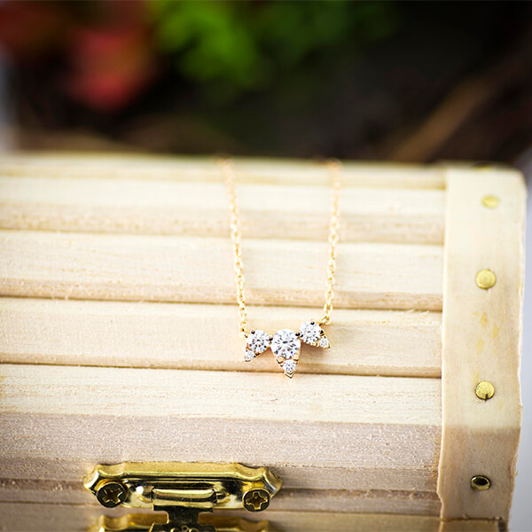 New yellow gold Hearts On Fire Aerial Triple Diamond necklace laid on wooden box.