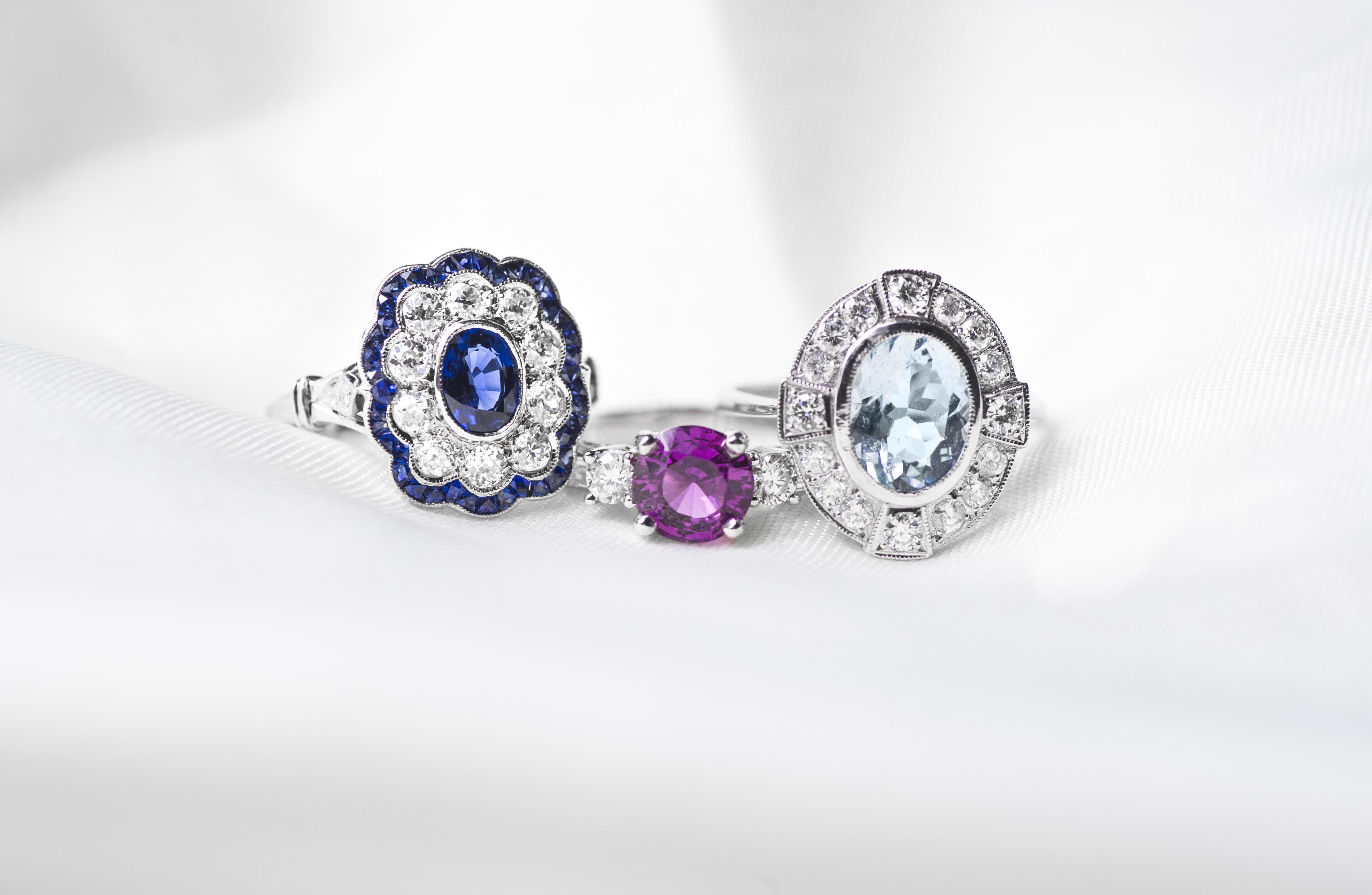 Three white gold engagement rings centered with colored gemstones on a white background.