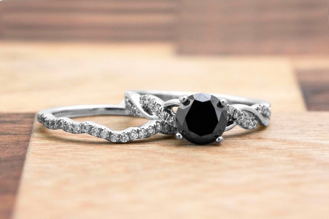 White gold twist shank engagement ring centered with a black diamond stacked on a white gold diamond eternity wedding band.