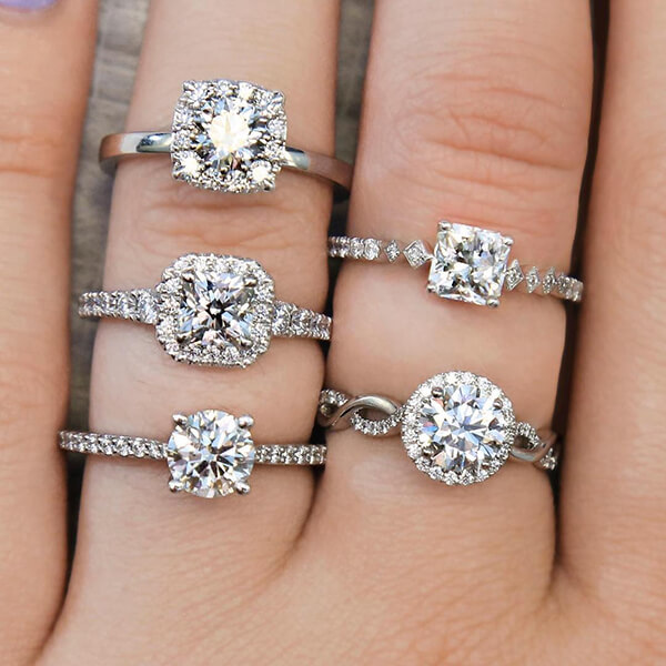 Five white gold diamond engagement rings with diamonds in the bands on woman’s
fingers.