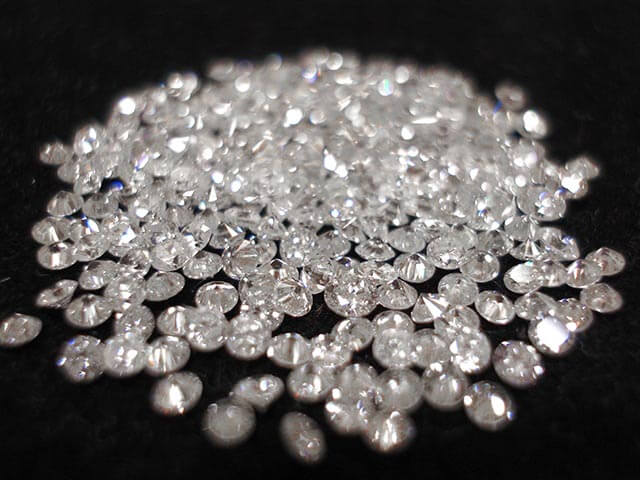 Pile of loose cut diamonds on black background.