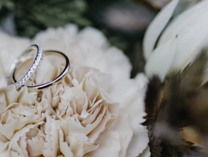 Two white gold wedding bands sitting on a white flower.