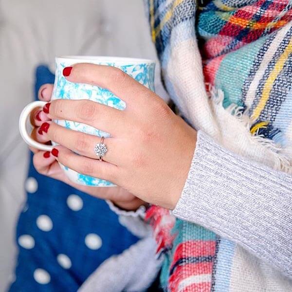 Woman holding coffee cup featuring her diamond engagement ring.