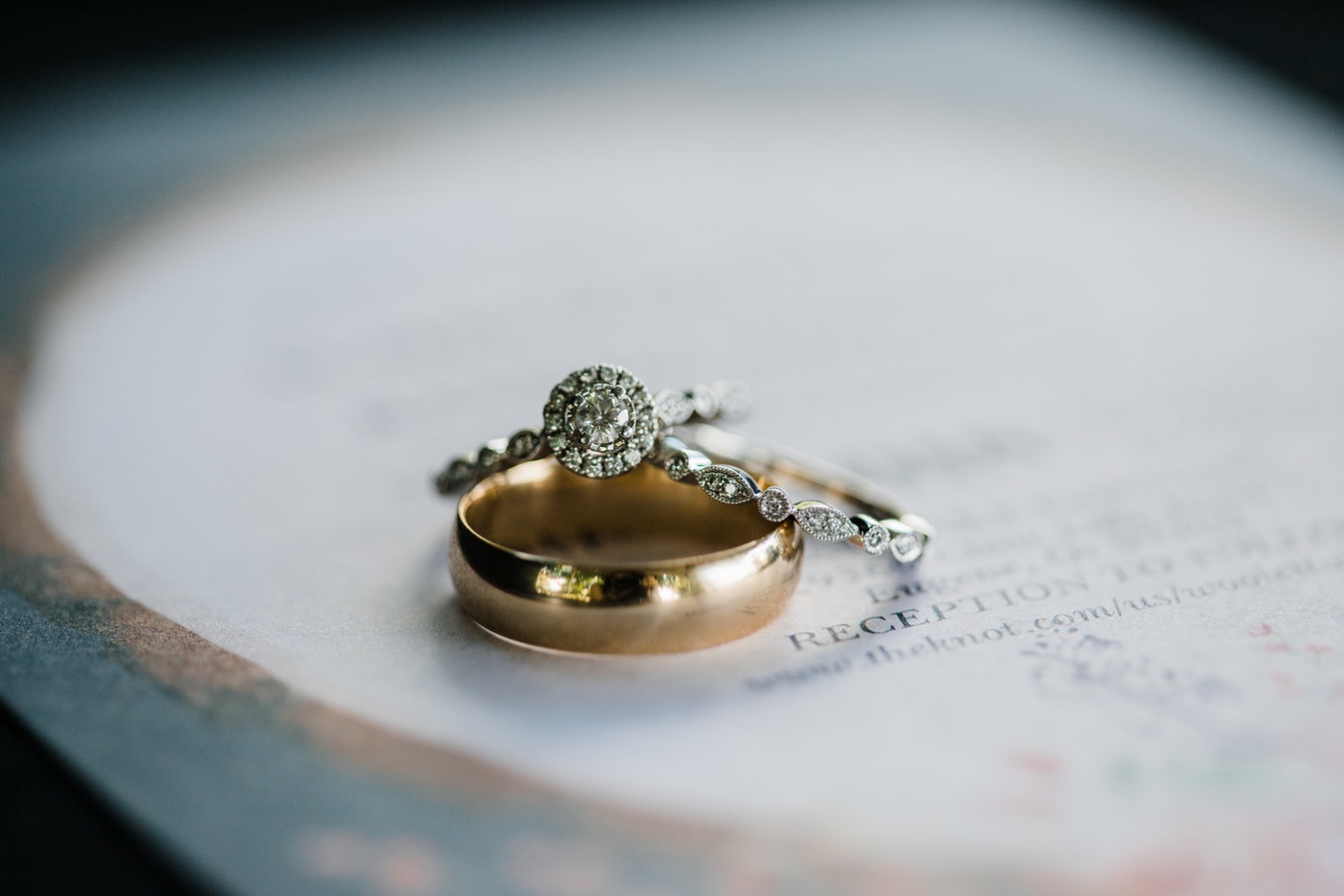 Two diamond engagement rings stacked on a yellow gold wedding band sitting on a white table.