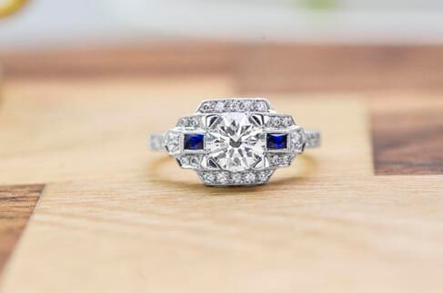 Platinum Art Deco diamond engagement ring surrounded by blue sapphires and diamonds.