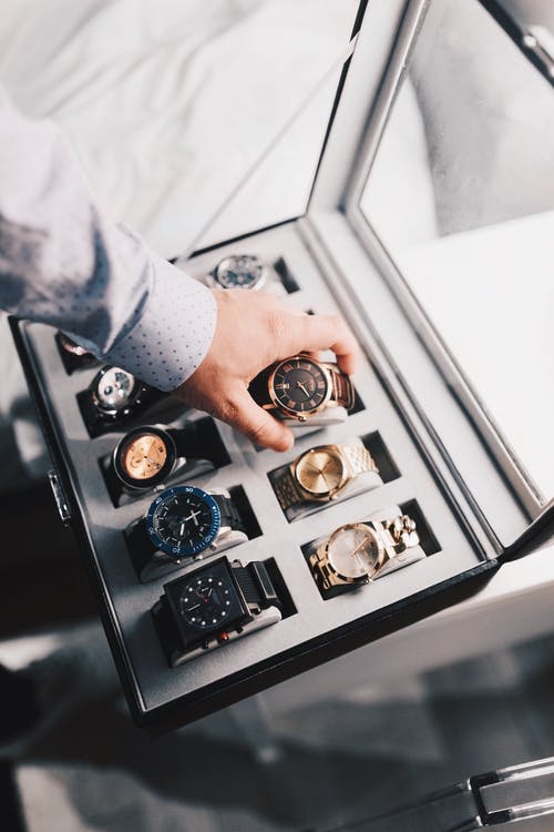 Man placing watch into watch storage box containing several other luxury watches.