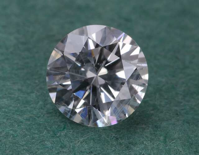 Loose round cut diamond on green background.