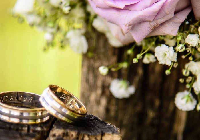 Two yellow and white gold layered wedding bands stacked on a wooden log next to a flower bouquet.