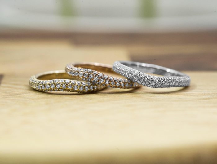 Yellow, rose, and white gold diamond eternity bands on a wooden table.
