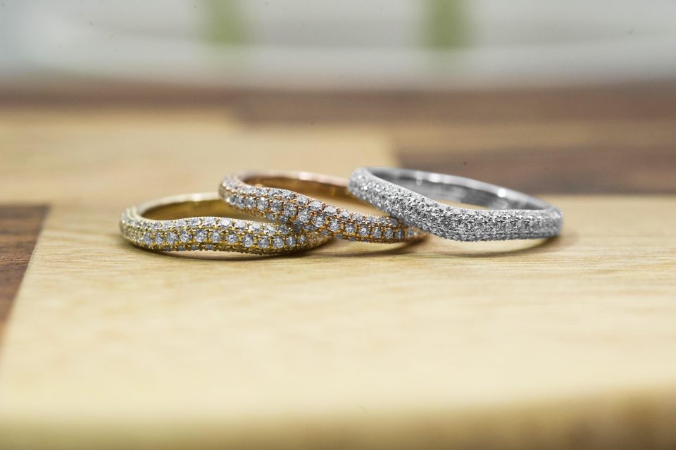 Yellow, rose, and white gold diamond eternity bands on a wooden table.