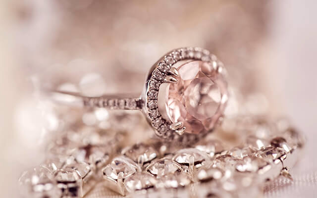 Rose gold ring centered with morganite surrounded by a diamond halo and diamonds in the band on top of various diamonds jewelry.