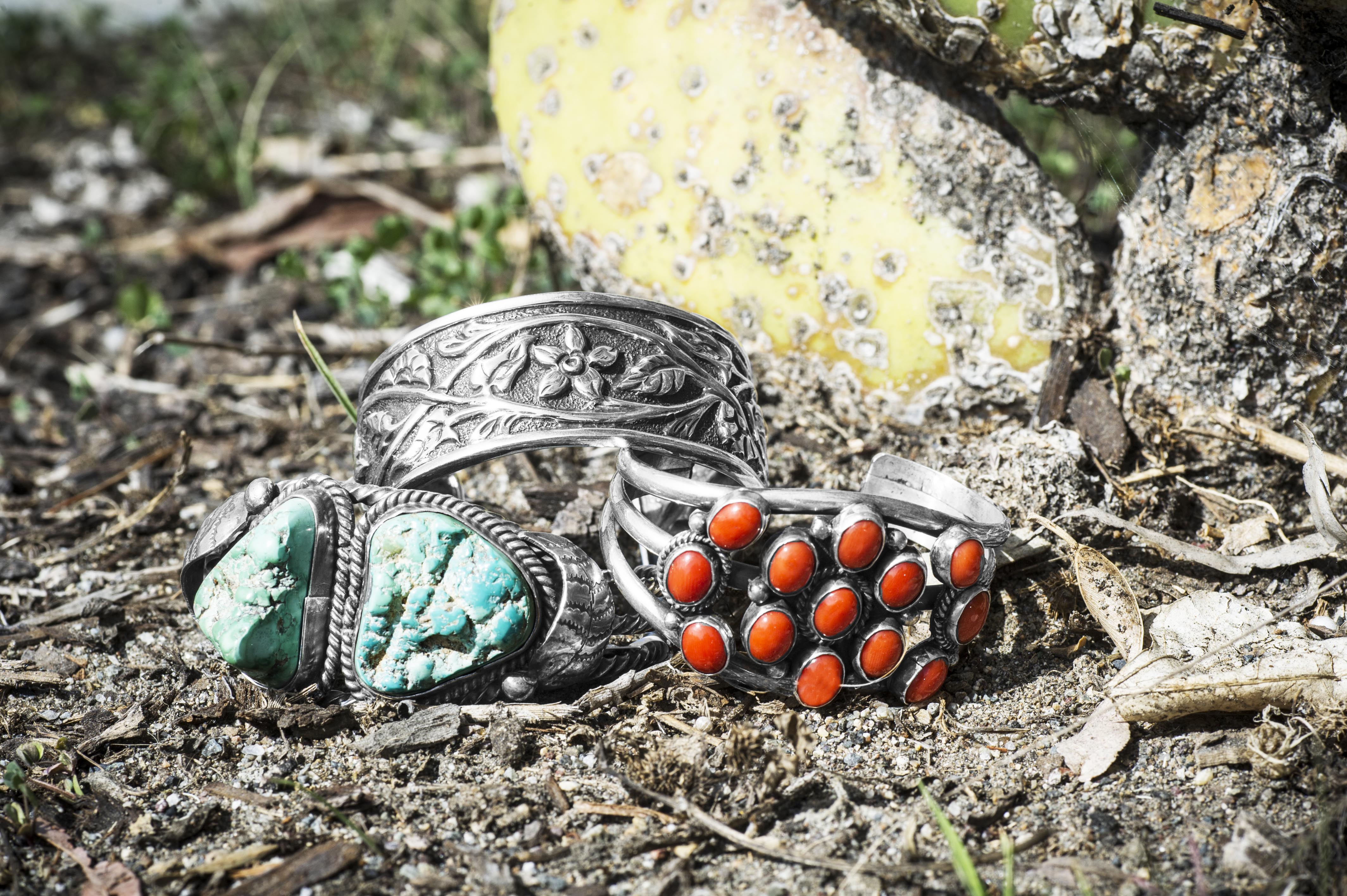 Three stacked sterling silver Native American cuff bracelets in outdoor scenery.