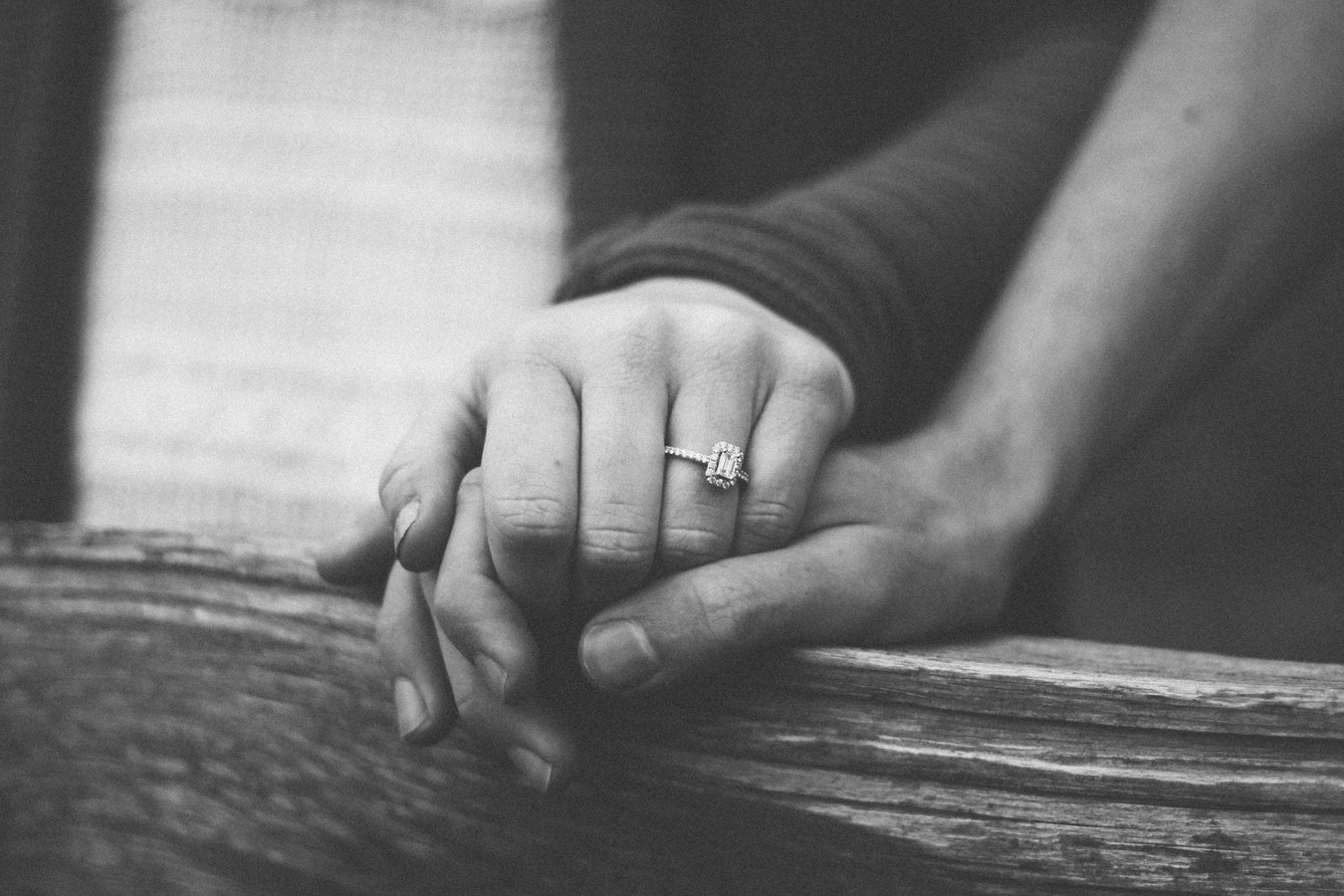 Black and white image of couple holding hands featuring diamond engagement ring.