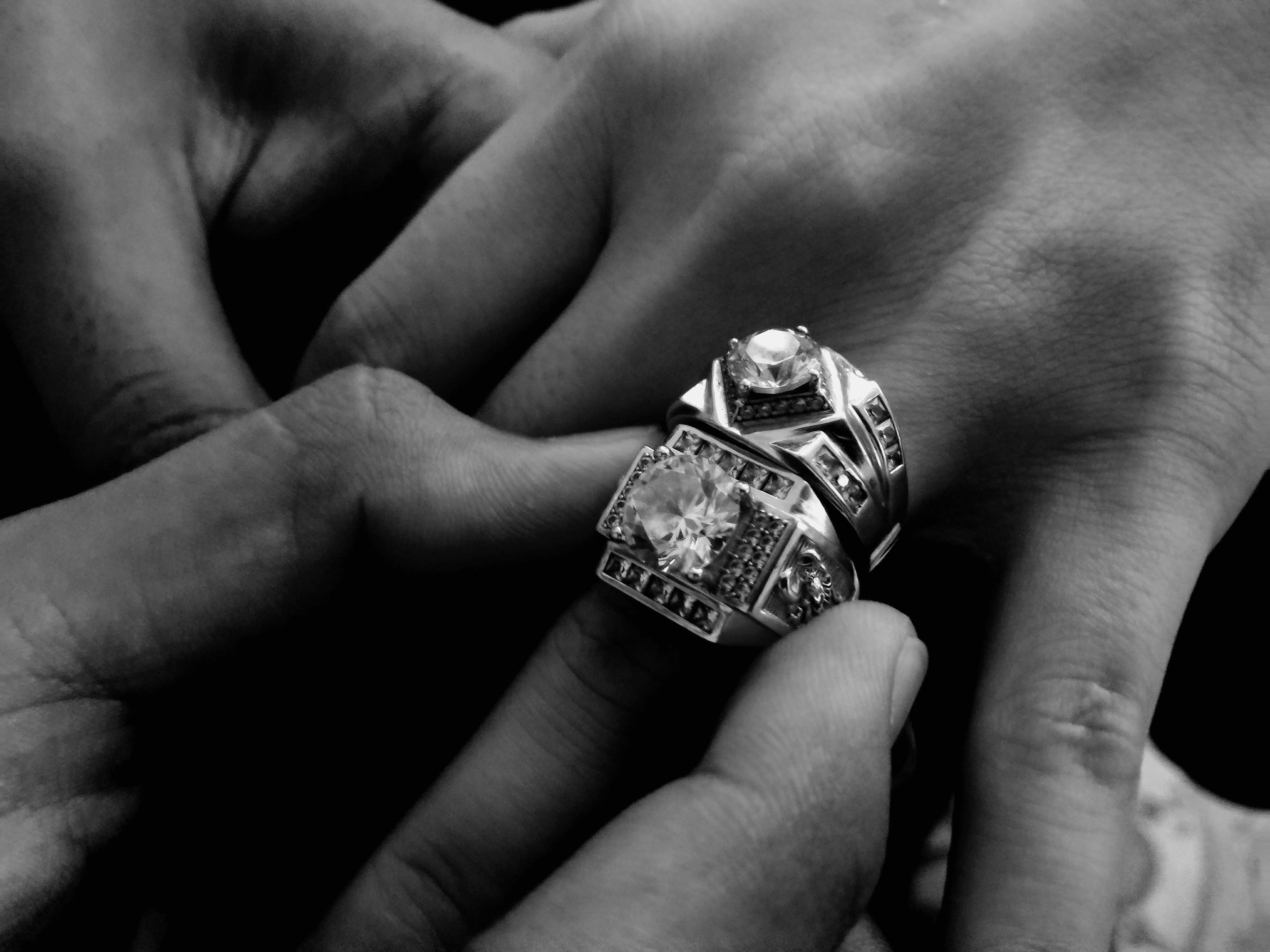 Man putting a diamond engagement ring onto a woman’s ring finger.