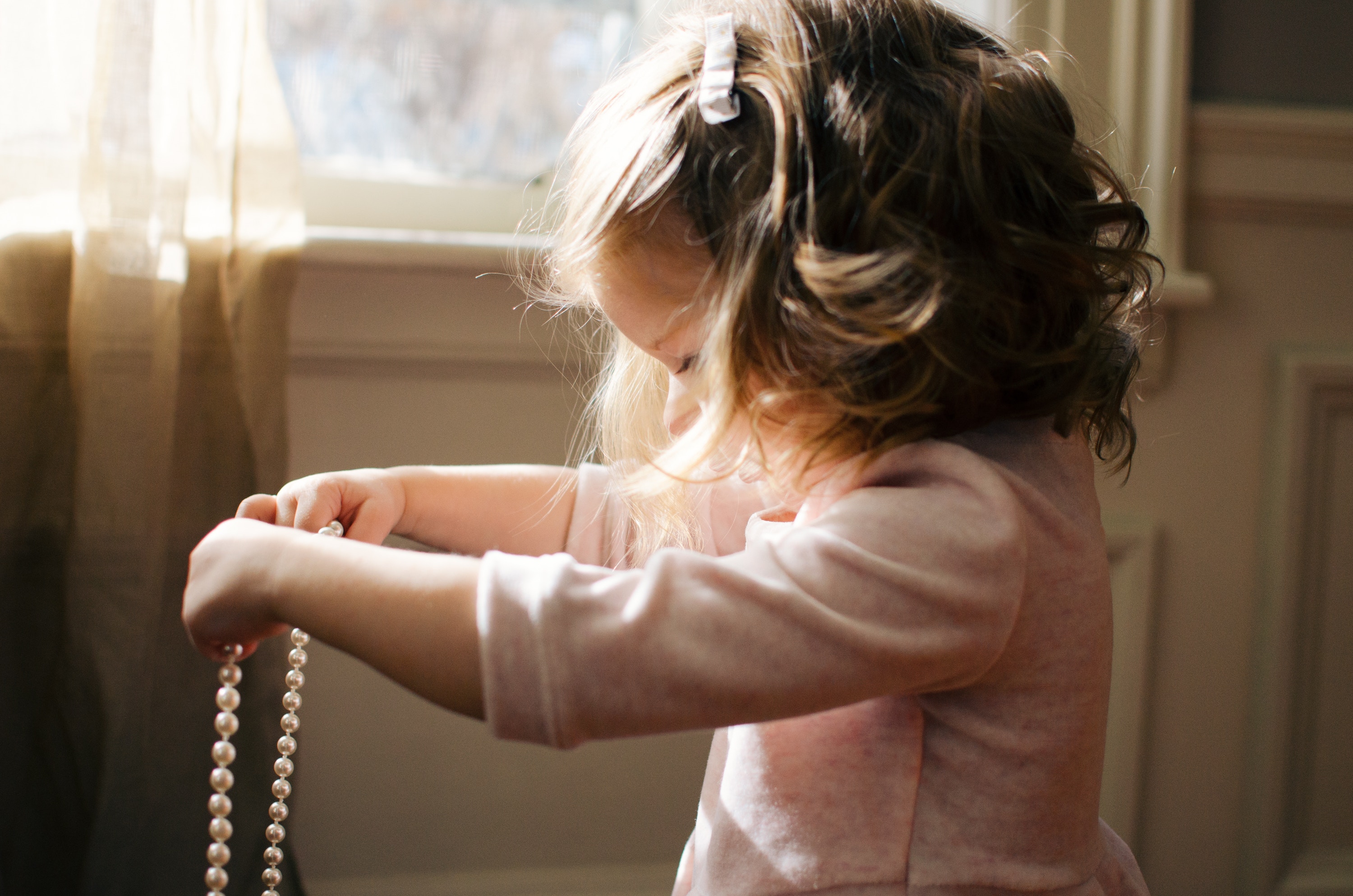 Child holding up a pearl strand necklace.