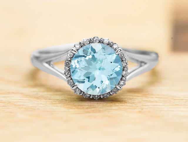 White gold engagement ring centered with an aquamarine surrounded by a diamond halo.