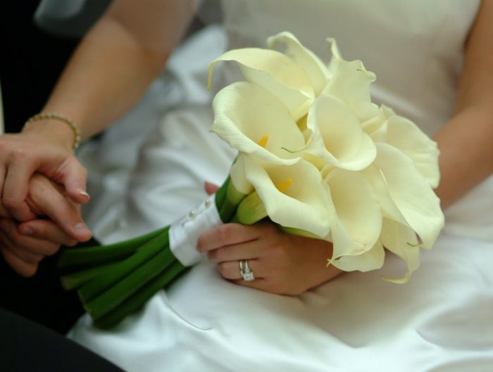 Bride holding flowers in one hand and groom’s hand in the other, featuring her diamond engagement ring and diamond bracelet.