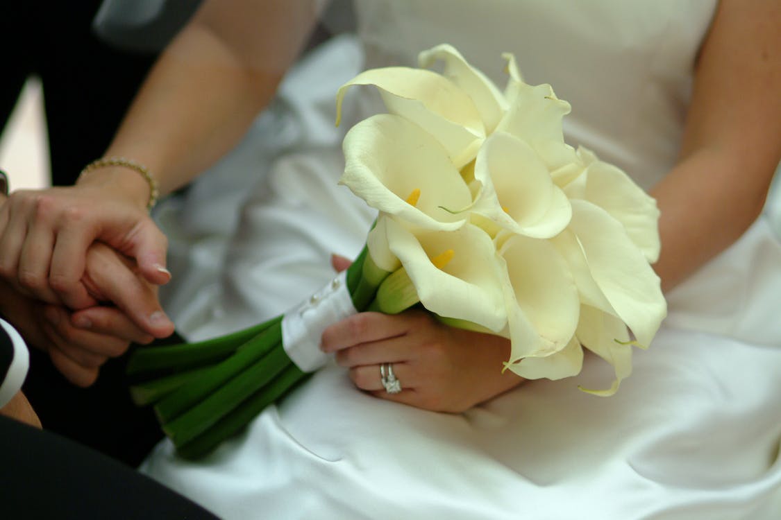 Bride holding flowers in one hand and groom’s hand in the other, featuring her diamond engagement ring and diamond bracelet.