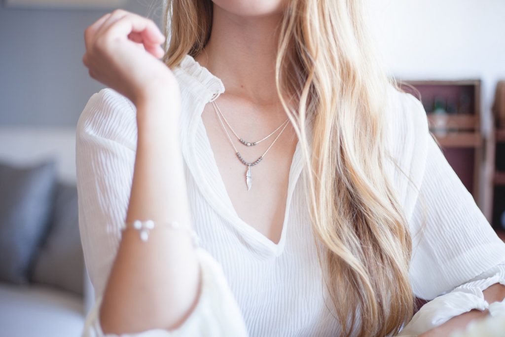 Woman in white button-up wearing a bracelet and layered necklaces.