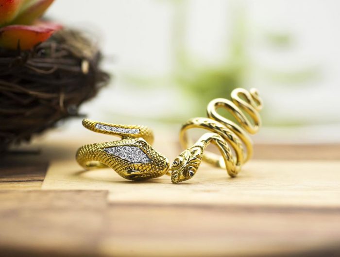 Two yellow gold snake rings on a wooden table.