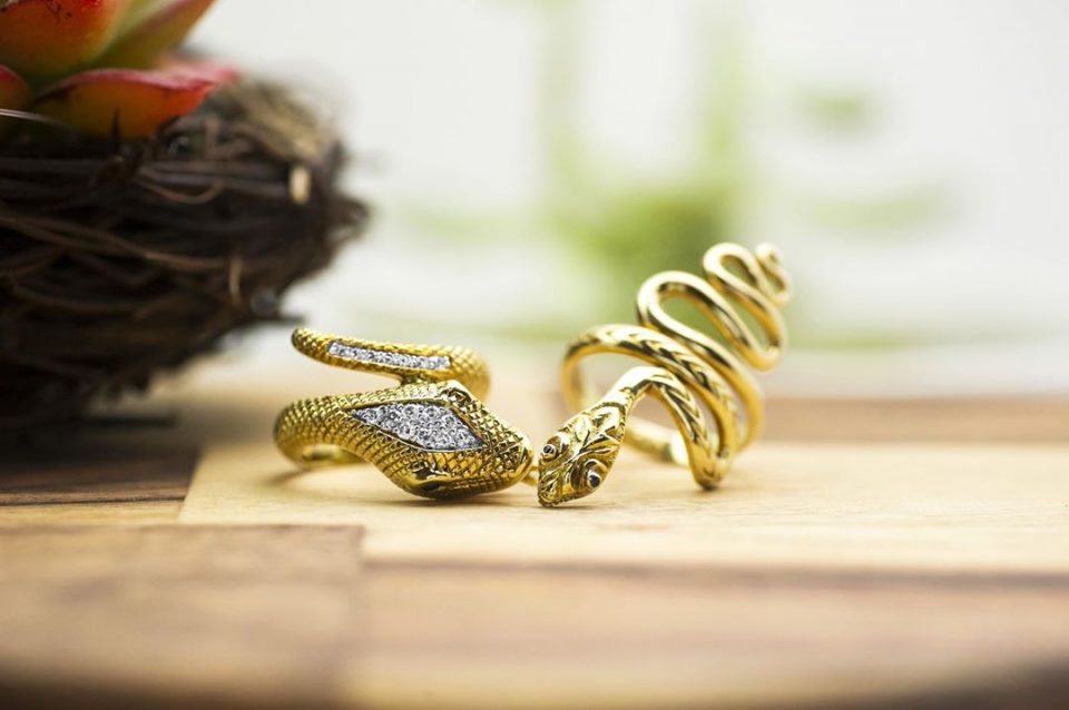 Two yellow gold snake rings on a wooden table.