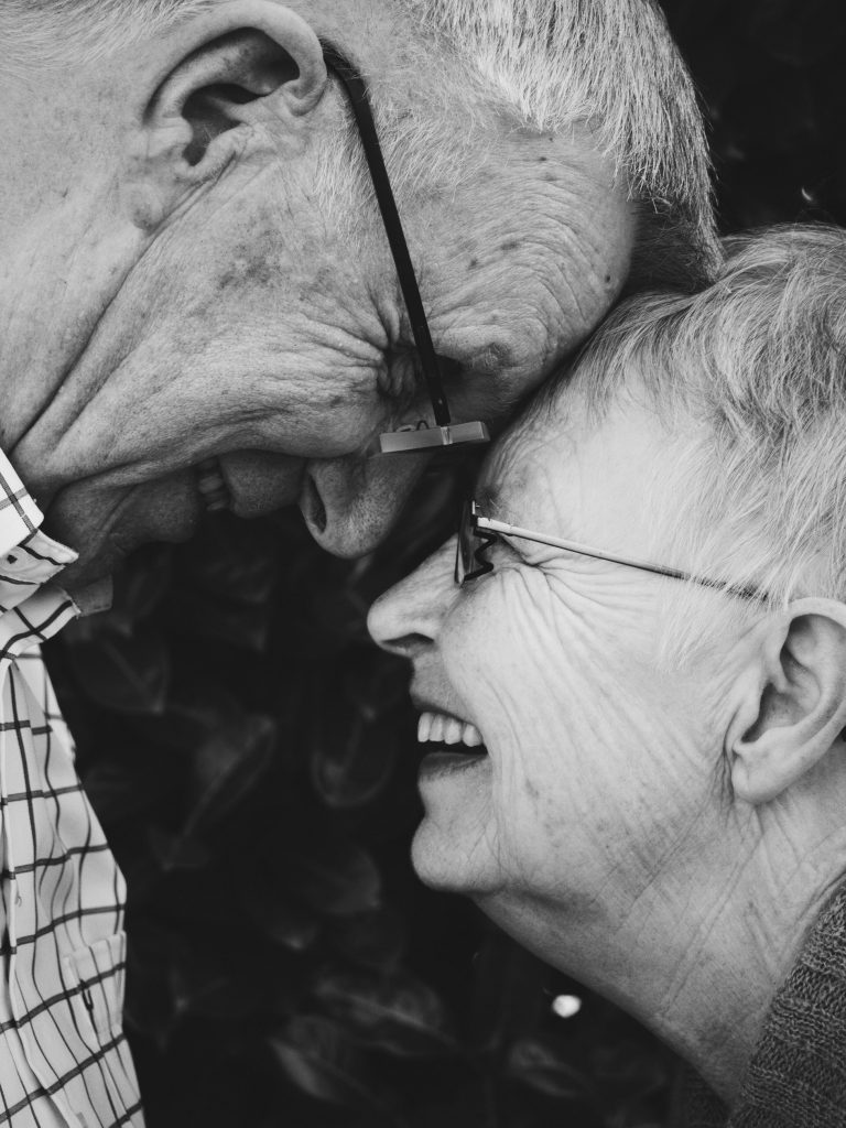 Older couple laughing with each other’s foreheads touching.