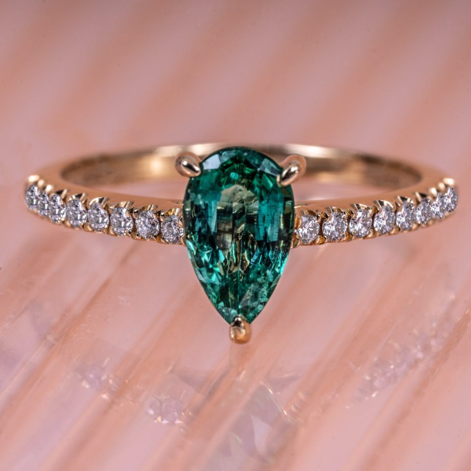 Yellow gold engagement ring centered with a pear cut emerald and diamonds in the band.