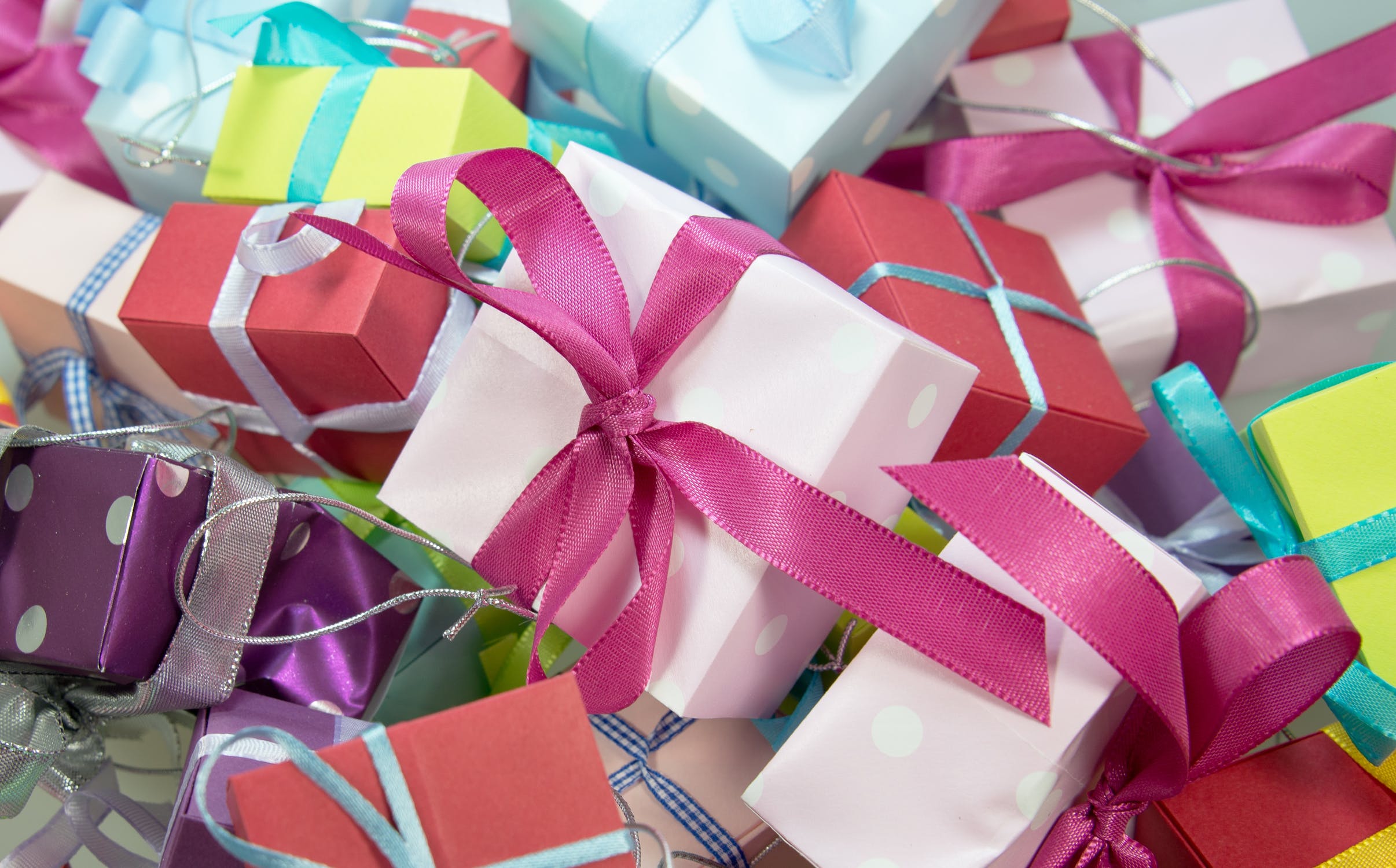 Stack of gift boxed wrapped in assorted neon paper and ribbons.