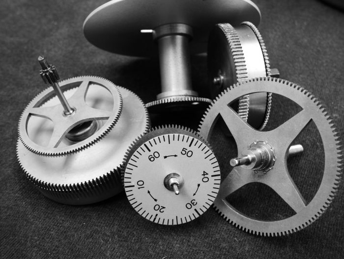 Various individual parts and gears of a watch on a black fabric background.