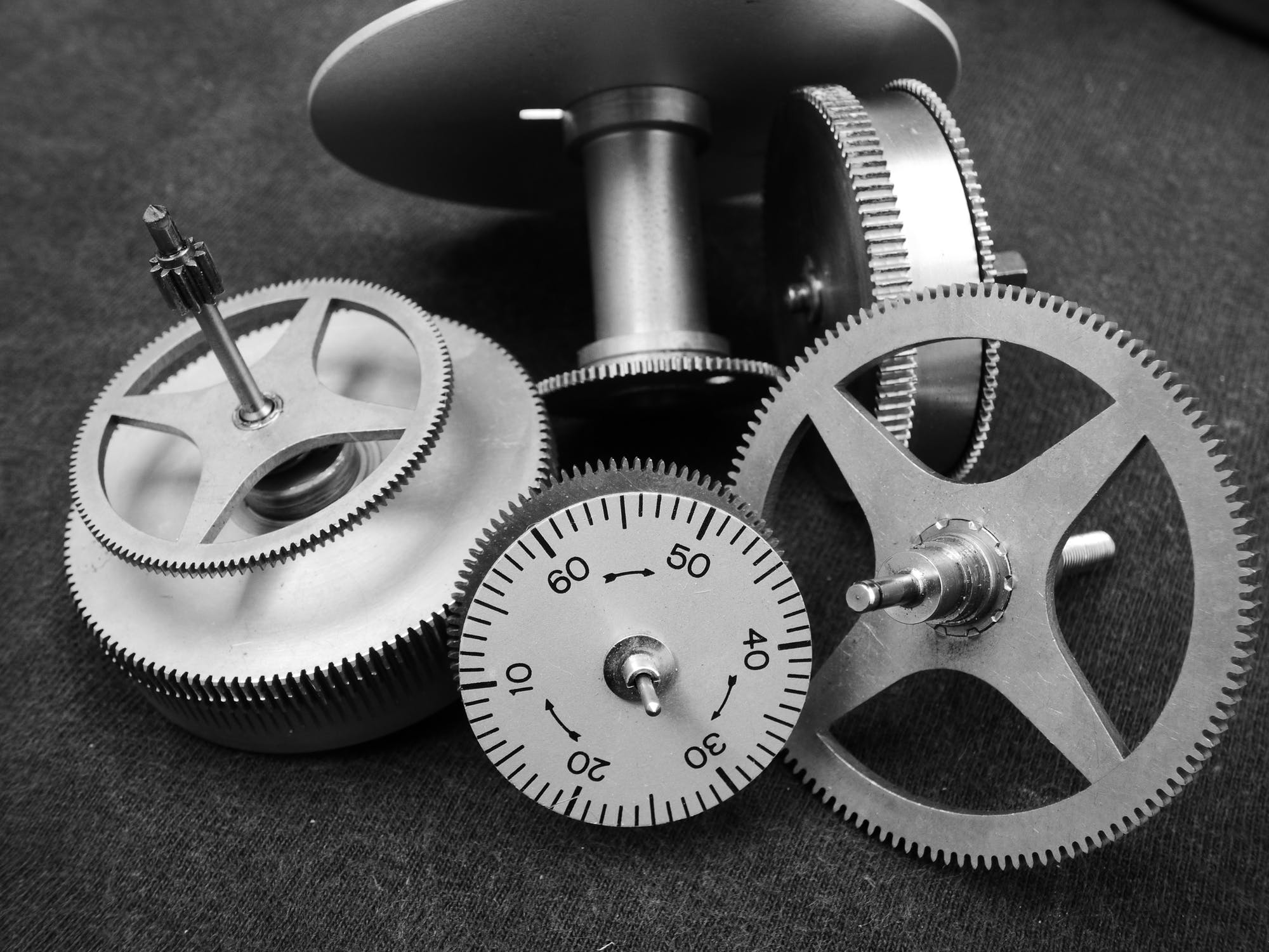 Various individual parts and gears of a watch on a black fabric background.