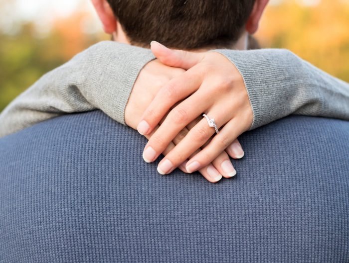 Woman’s arms wrapped around man’s neck showing off her diamond engagement ring.