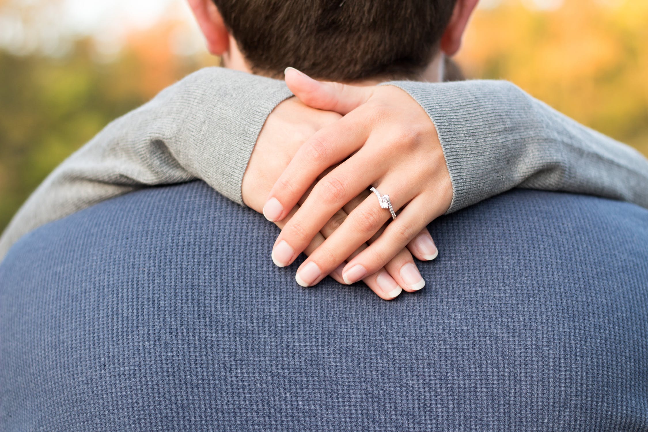 Woman’s arms wrapped around man’s neck showing off her diamond engagement ring.