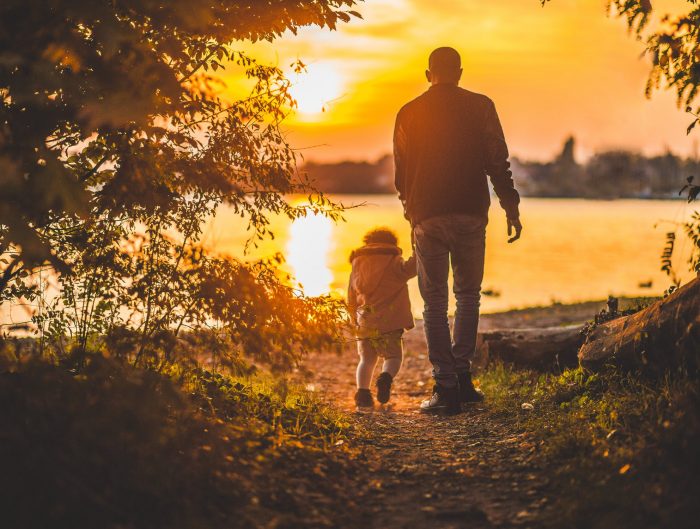 Father and child walking towards lake at sunset.