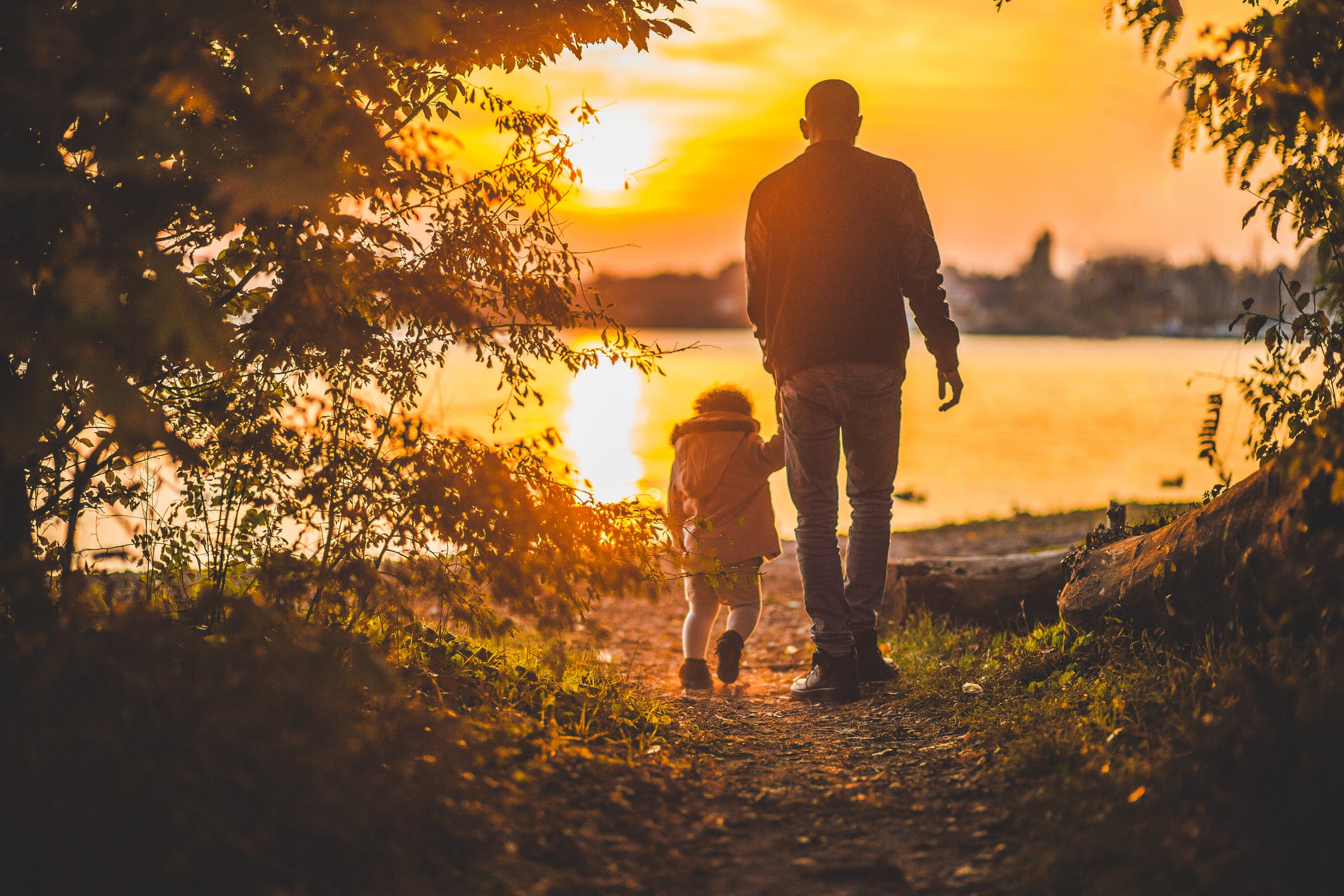 Father and child walking towards lake at sunset.