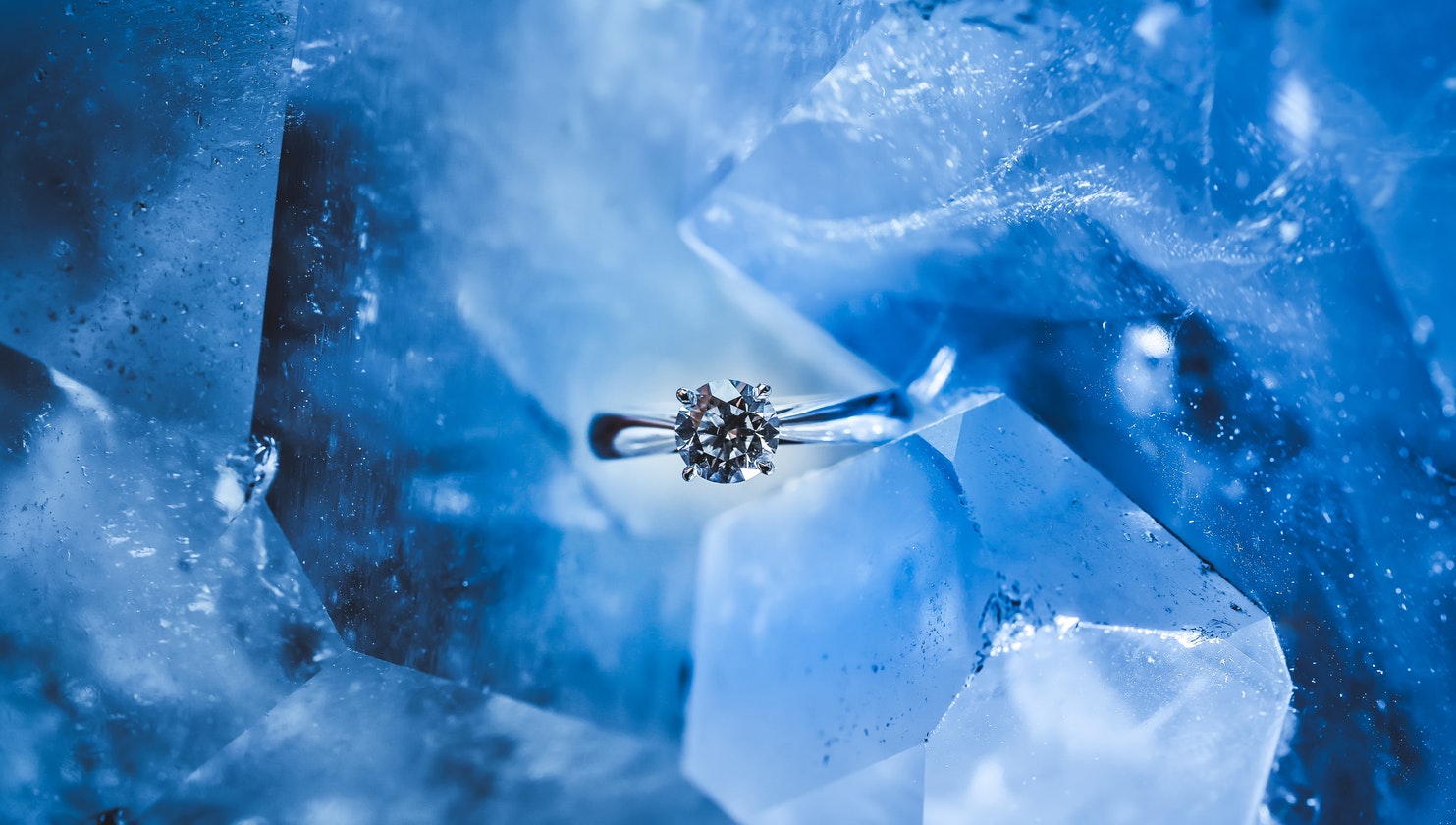 White gold solitaire engagement ring centered with a diamond on a blue ice background.