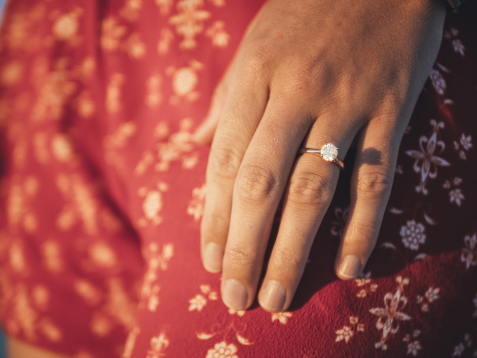 Woman’s hand featuring solitaire diamond engagement ring.